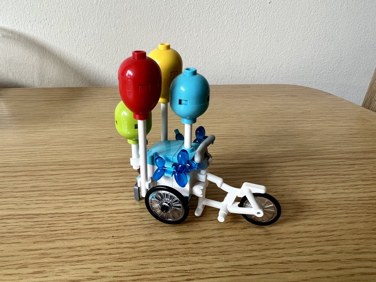 A balloon cart attached to the back of a bicycle. There are four classic round balloons and two translucent blue balloon dogs