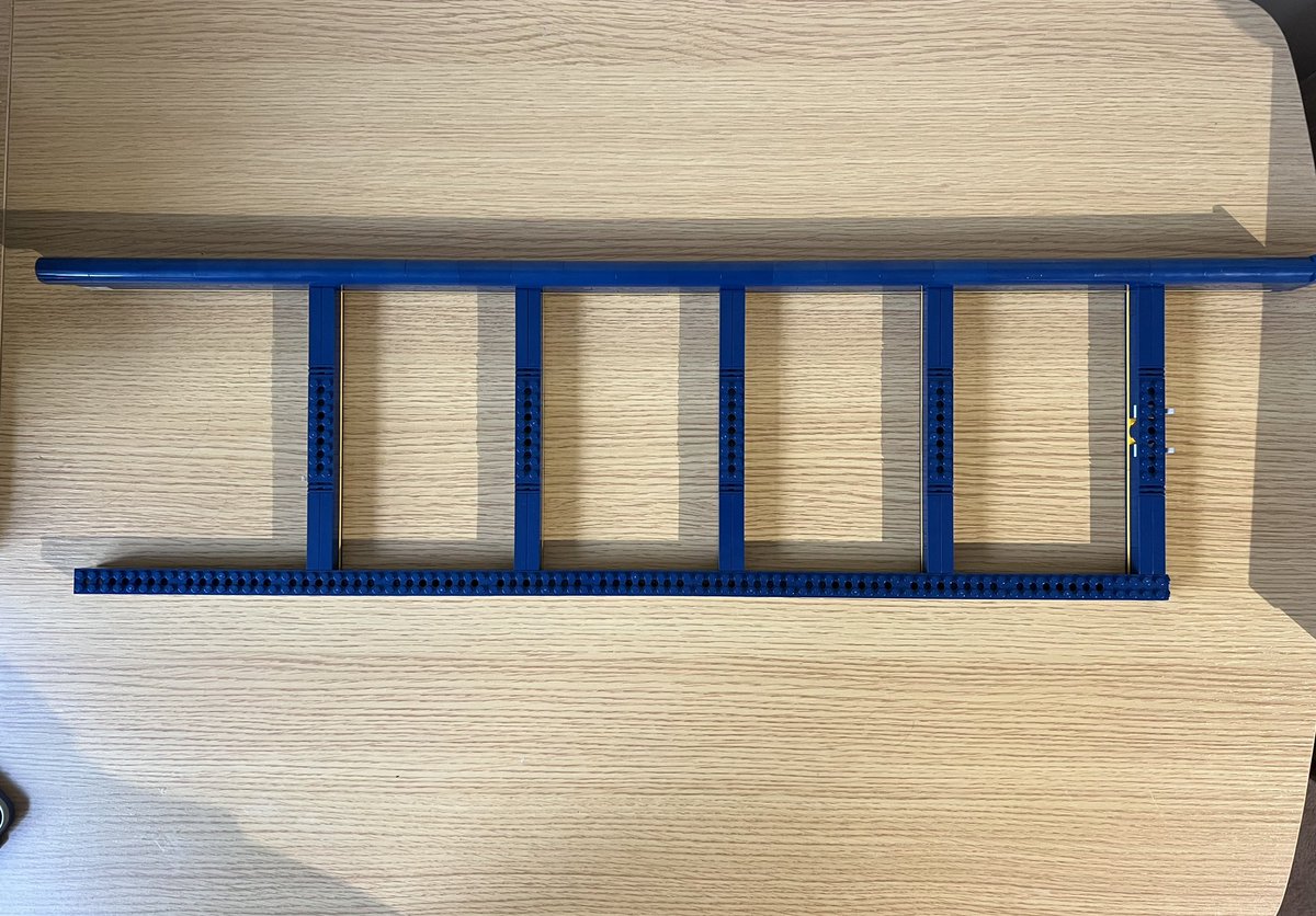 A dark blue ladder shape made from lego seen from above laying flat on a desk