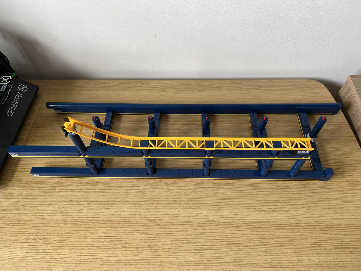 A lego structure that looks like a blue ladder with yellow roller coaster track down one side.