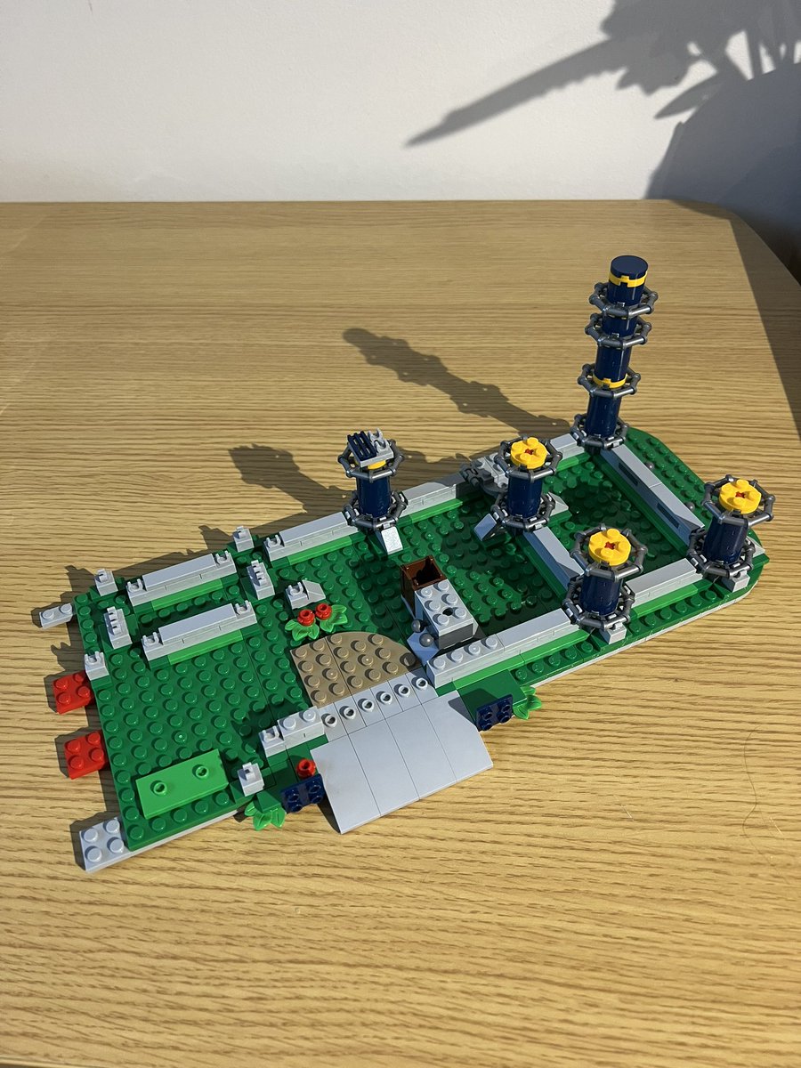 A partially built lego set. There’s a green base with grey railings, and dark blue poles sticking up from where the railings meet