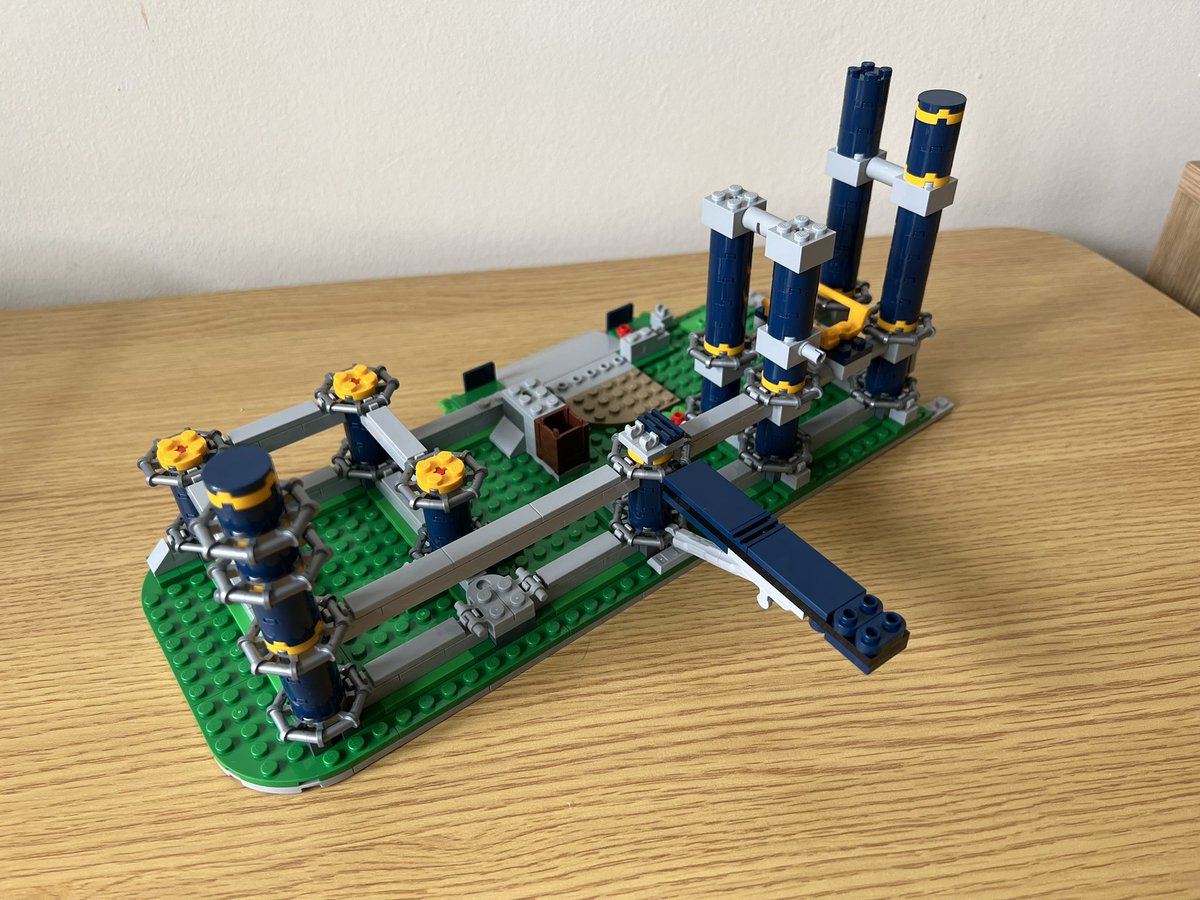 A partially built lego roller coaster that only has a few supports on a green base. One of the support poles has a horizontal strut attached that extends outwards off the base