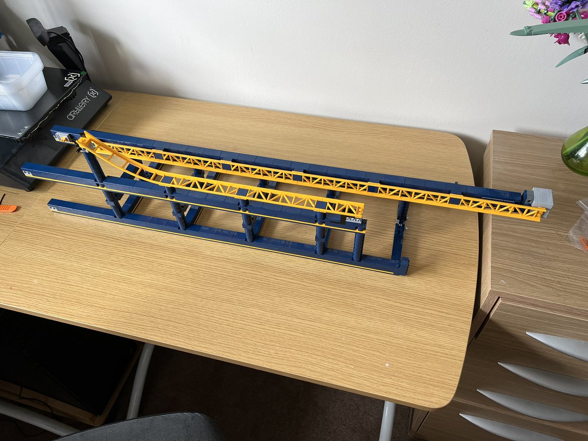 A lego structure that looks like a blue ladder with yellow roller coaster track down two sides