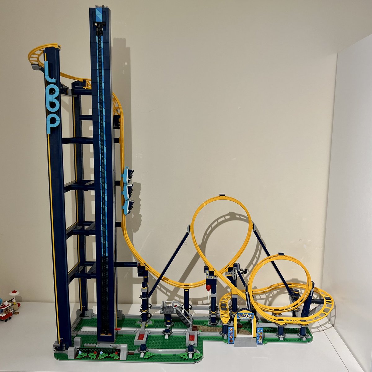 A lego roller coaster with dark blue supports and yellow track. It has two loops on the right and a tall tower on the left.