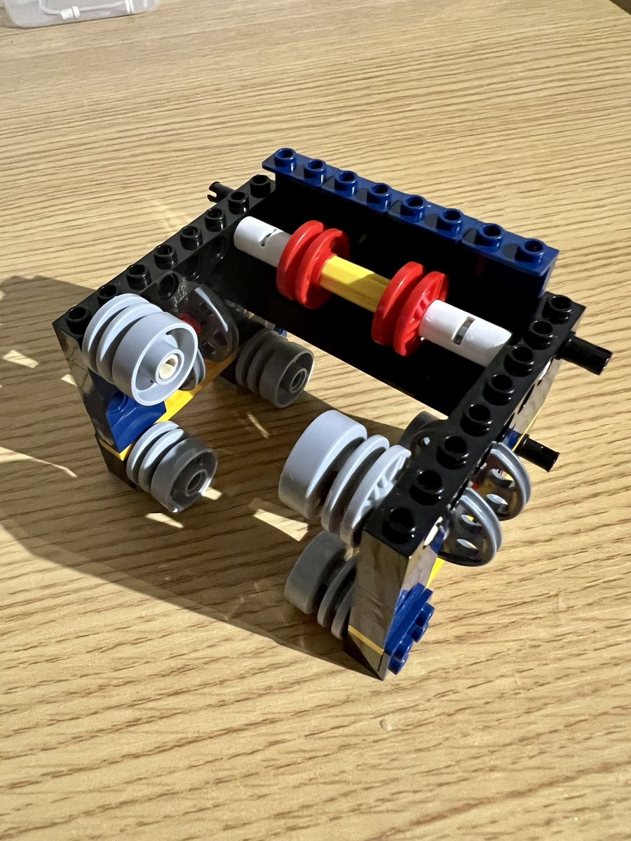 A small lego structure with four wheels on the bottom, two sets of thinner wheels in the middle, and a pair of red and a pair of grey wheels at the top.