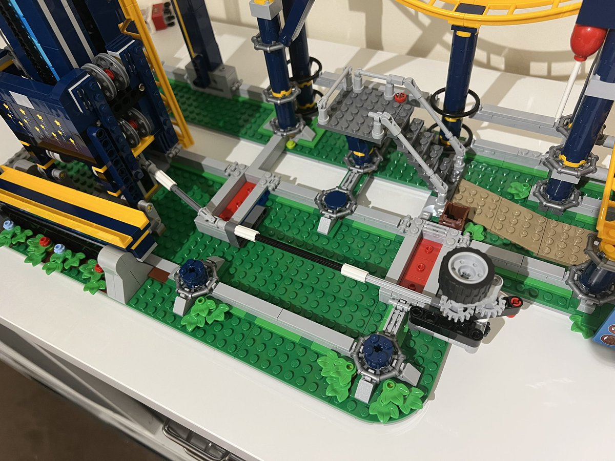 A closeup of a lego roller coaster showing a tyre on its side connected up to the chain lift using a series of axles.