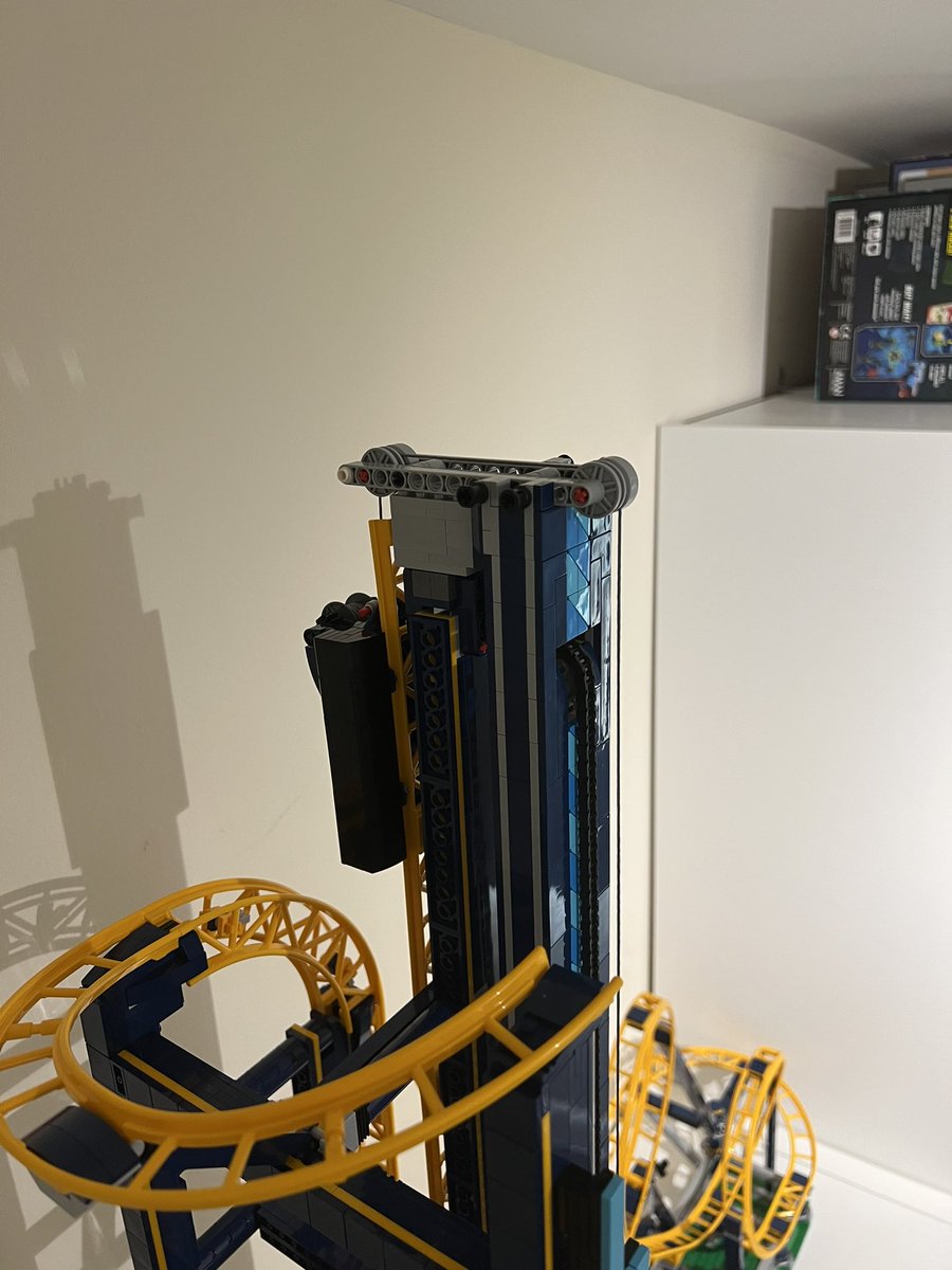 A closeup at the top of the tower on a lego roller coaster. There’s a pulley mechanism and a black block acting as a counterweight.