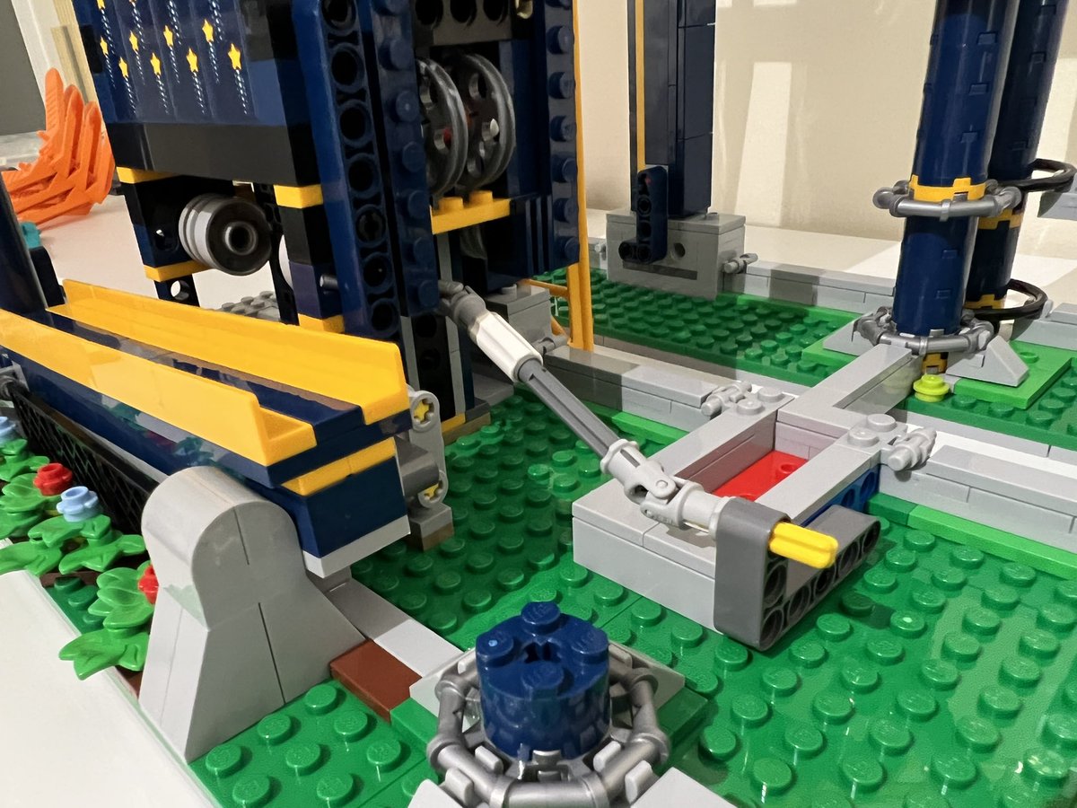 A closeup of the base of a lego roller coaster. There’s an axle connected to the bottom of a chain lift and extending out into the open.