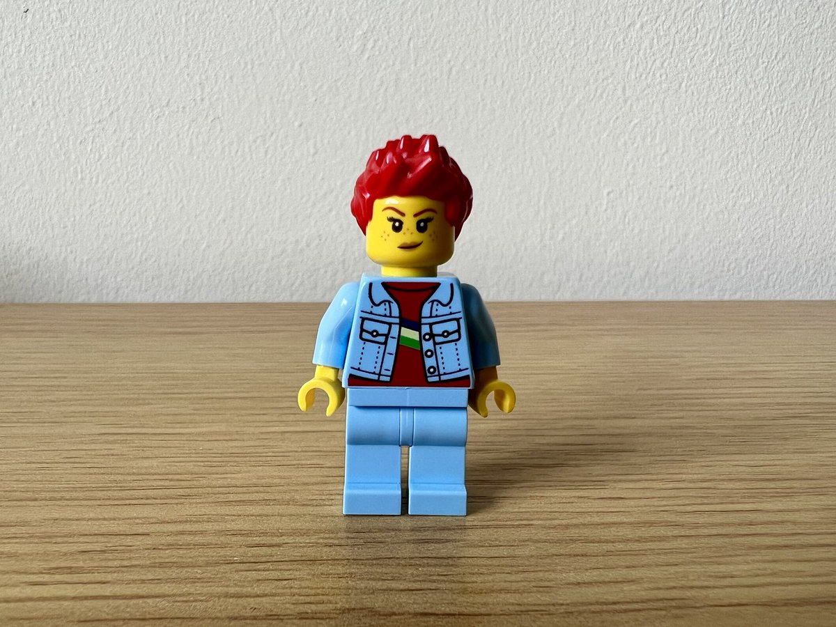 A lego minifigure with bright red short spiky hair, a denim jacket, and denim trousers. They have pale pink lipstick and freckles.