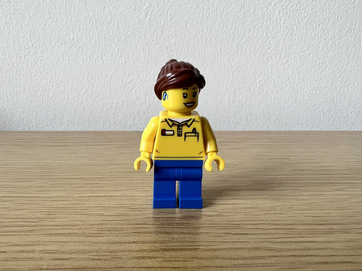 A lego minifigure in a yellow polo top and blue trousers. She has what looks like a hearing aid on the side of her head.