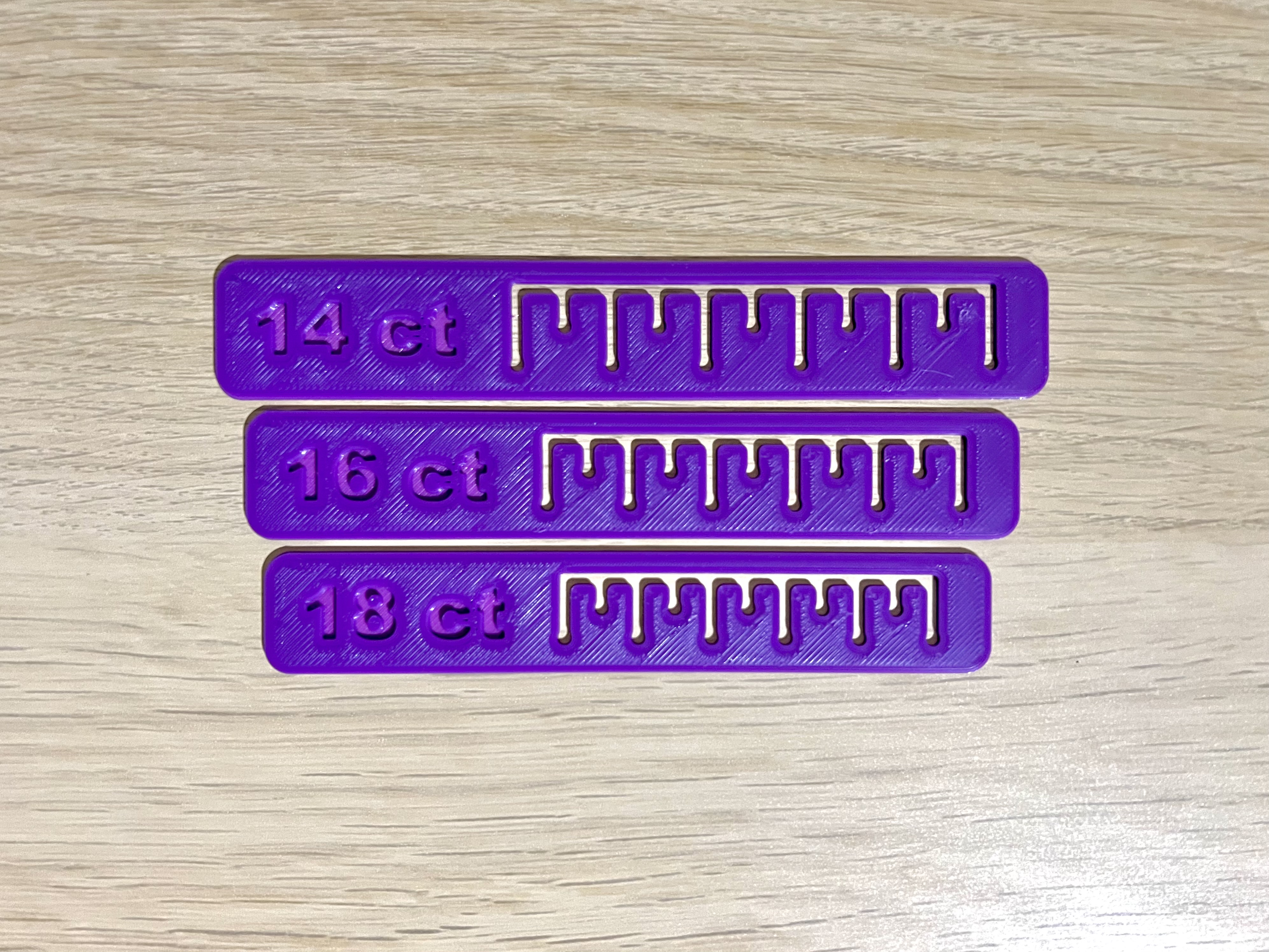 Three purple rulers in a vertical line. Each one has a cutout that looks like tickmarks on a number line, and they're engraved with "14 ct", "16 ct", and "18 ct".