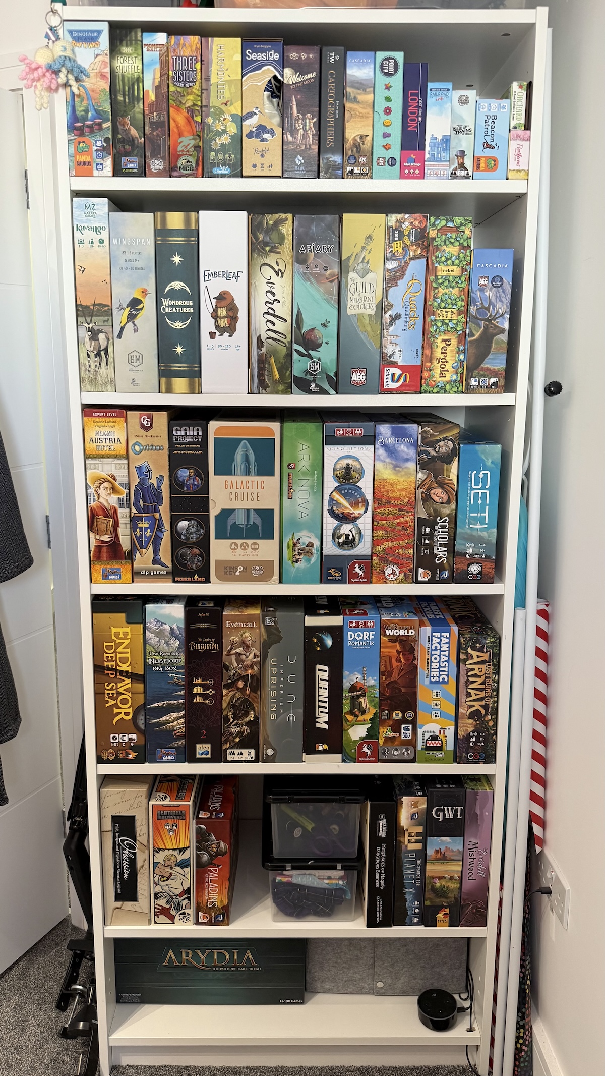 A tall white bookcase that has 6 shelves filled with board games.